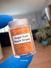 Load image into Gallery viewer, Jar of 'Sugar Rush Peach Stripey' spice blend held by a gloved hand in a home setting.