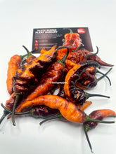 Load image into Gallery viewer, Black Panther peppers with a &#39;Tasty Pepper Plant Nursery&#39; sign in the background.
